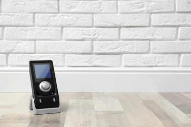 Modern audio speaker remote on floor near white brick wall. Space for text