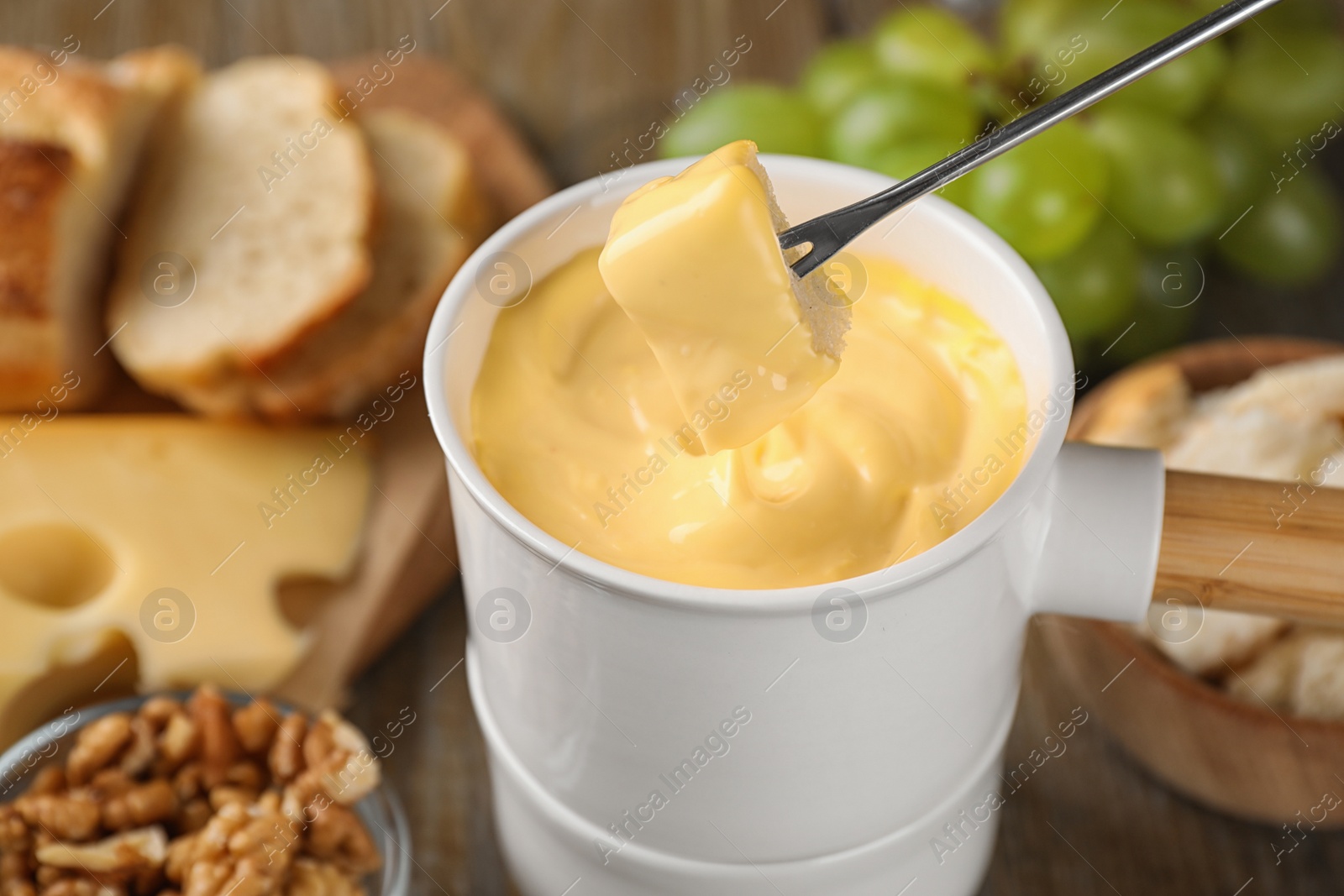 Photo of Dipping piece of cheese into tasty cheese fondue on table, closeup view