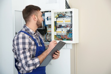 Photo of Male electrician with clipboard near fuse board indoors, space for text