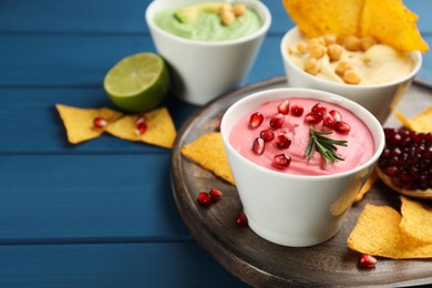 Photo of Bowl of delicious pink hummus with rosemary and pomegranate seeds on blue wooden table. Space for text