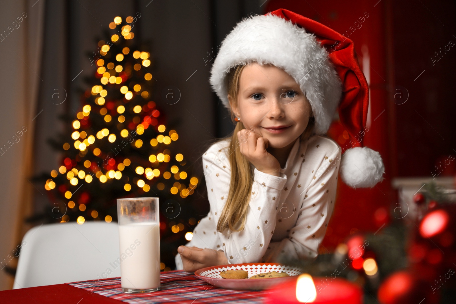 Photo of Cute little child with milk and cookies at table in dining room. Christmas time