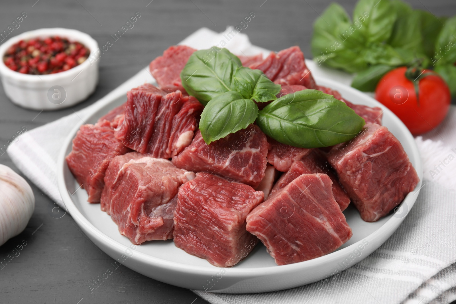 Photo of Cut fresh beef meat with basil leaves on grey table, closeup