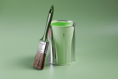 Photo of Can of paint and brush on light green background