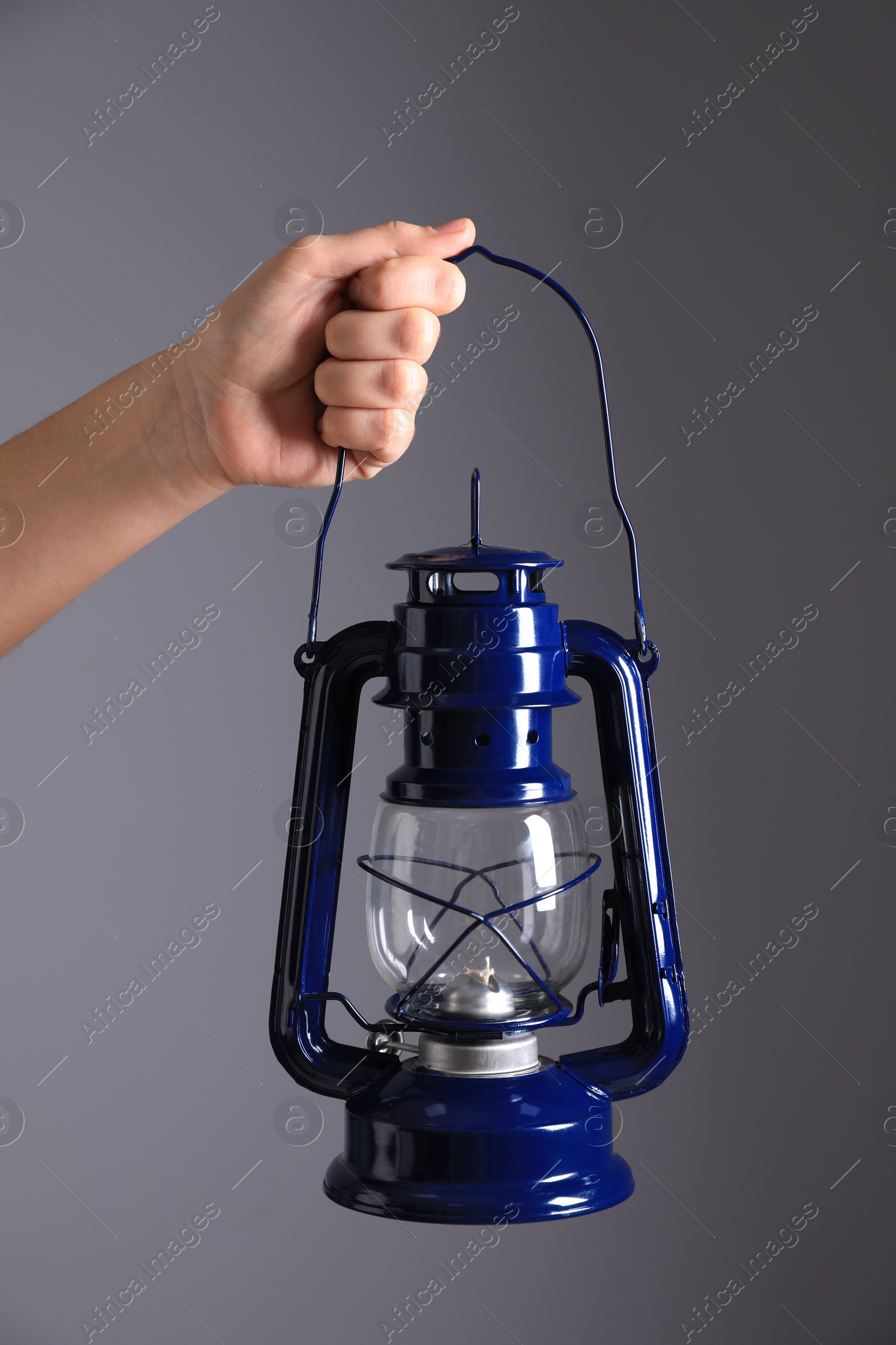 Photo of Woman holding blue kerosene lamp on grey background, closeup