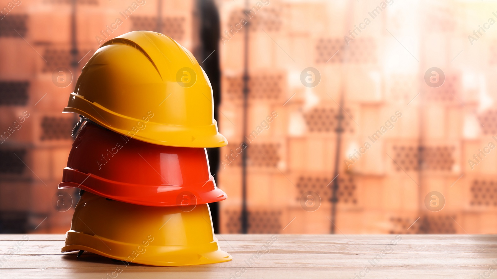 Image of Hard hats on wooden surface near pallets with red bricks. Space for text