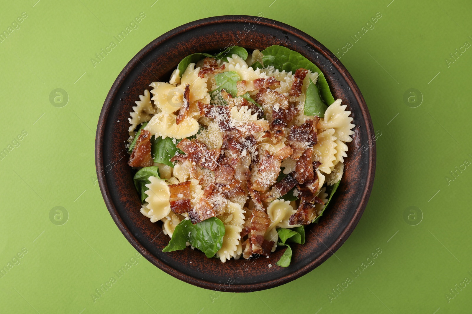 Photo of Tasty pasta with bacon and basil on light green table, top view