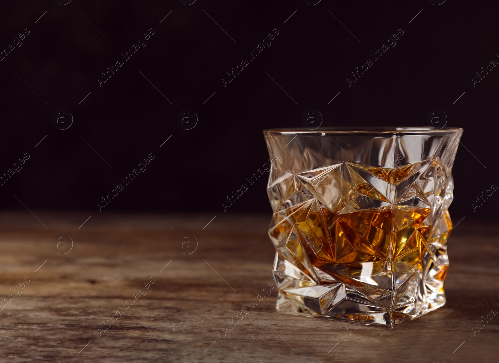 Photo of Golden whiskey in glass with ice cubes on table. Space for text