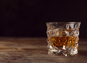 Golden whiskey in glass with ice cubes on table. Space for text