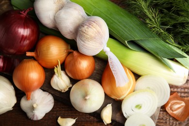 Photo of Fresh onion bulbs, leeks, garlic on wooden table, flat lay