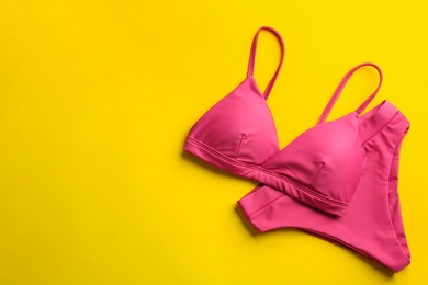 Beautiful pink bikini on yellow background, top view. Space for text