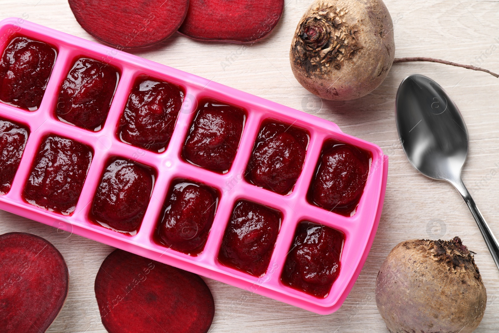Photo of Beet puree in ice cube tray on white wooden table, flat lay. Ready for freezing