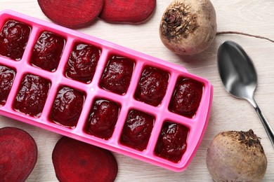 Photo of Beet puree in ice cube tray on white wooden table, flat lay. Ready for freezing