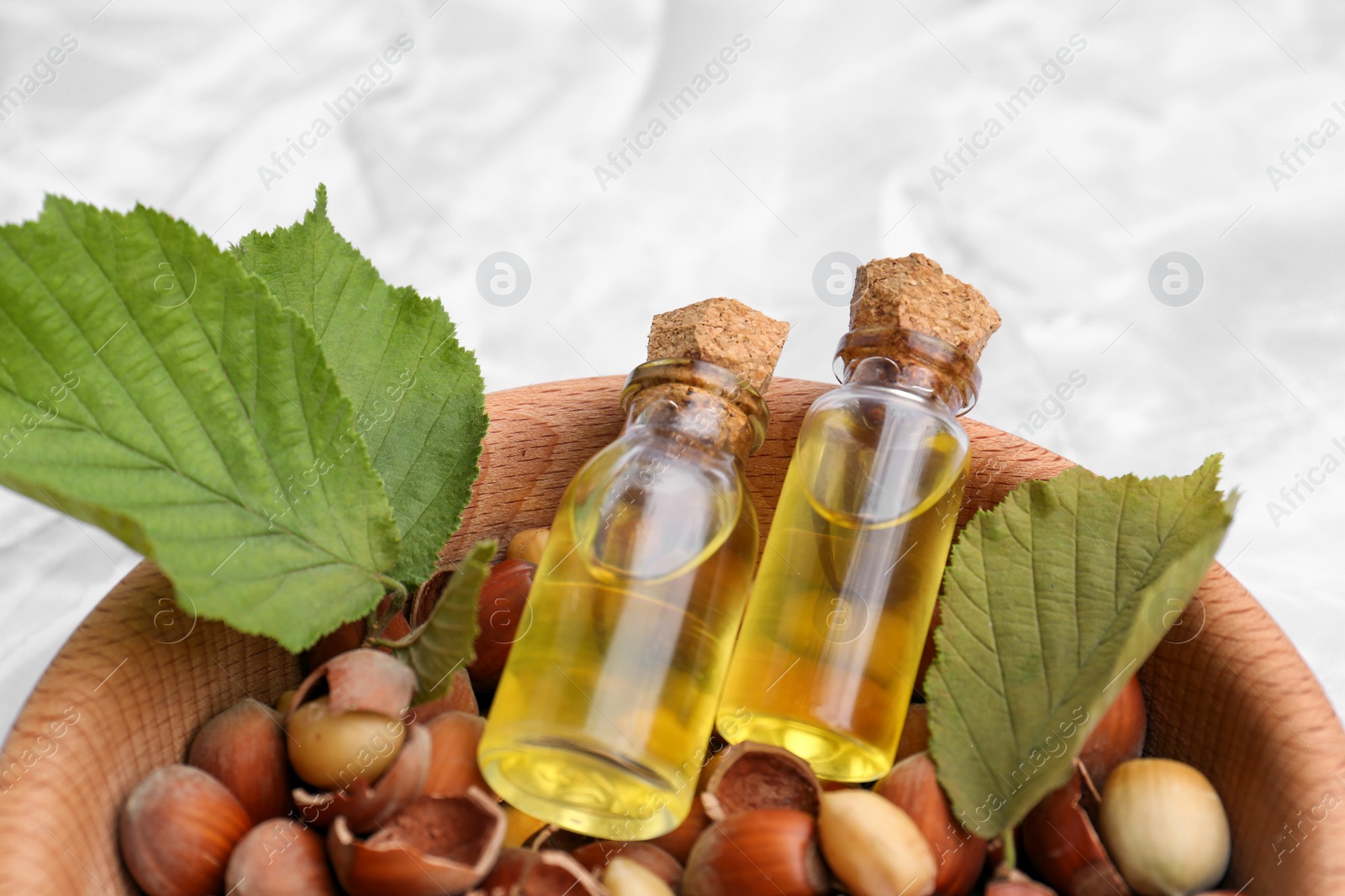 Photo of Bottles of hazelnut essential oil and nuts in wooden bowl, closeup