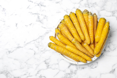 Photo of Many raw yellow carrots on white marble table, top view. Space for text