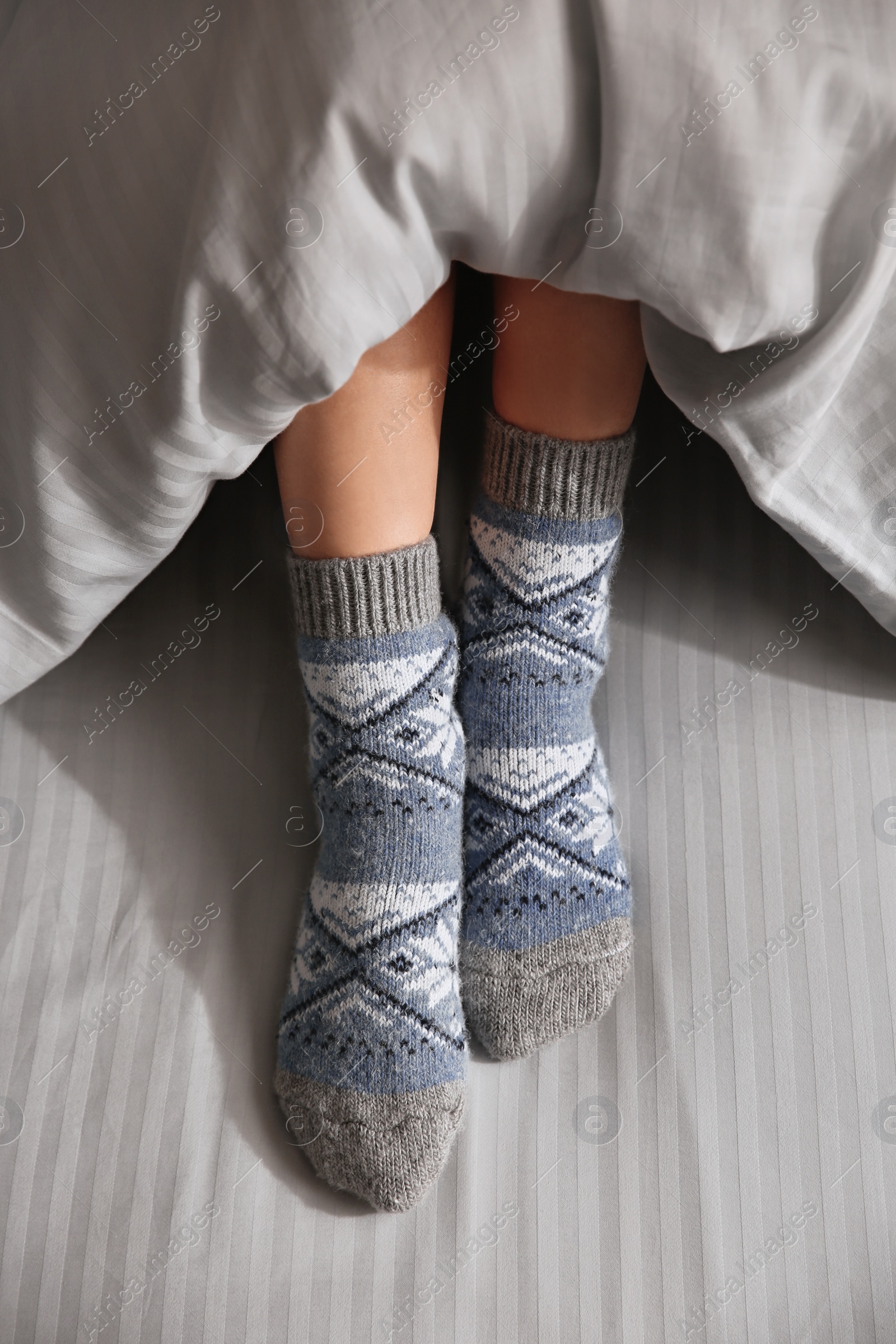 Photo of Woman wearing knitted socks under blanket in bed, closeup