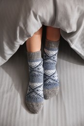 Woman wearing knitted socks under blanket in bed, closeup