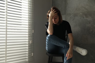 Sad young woman sitting on chair indoors, space for text