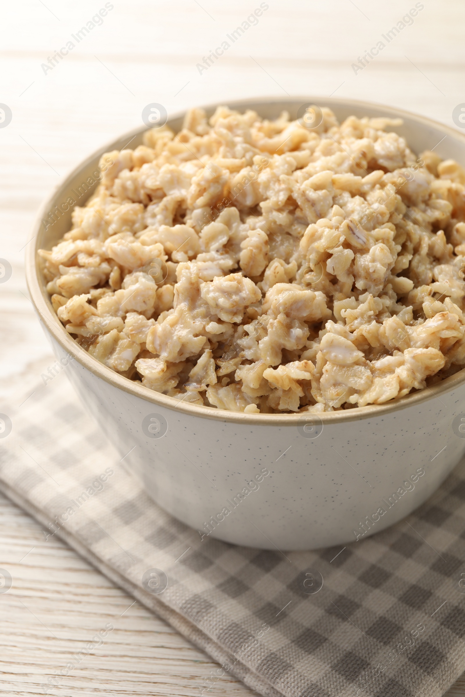 Photo of Tasty boiled oatmeal in bowl on light wooden table, closeup