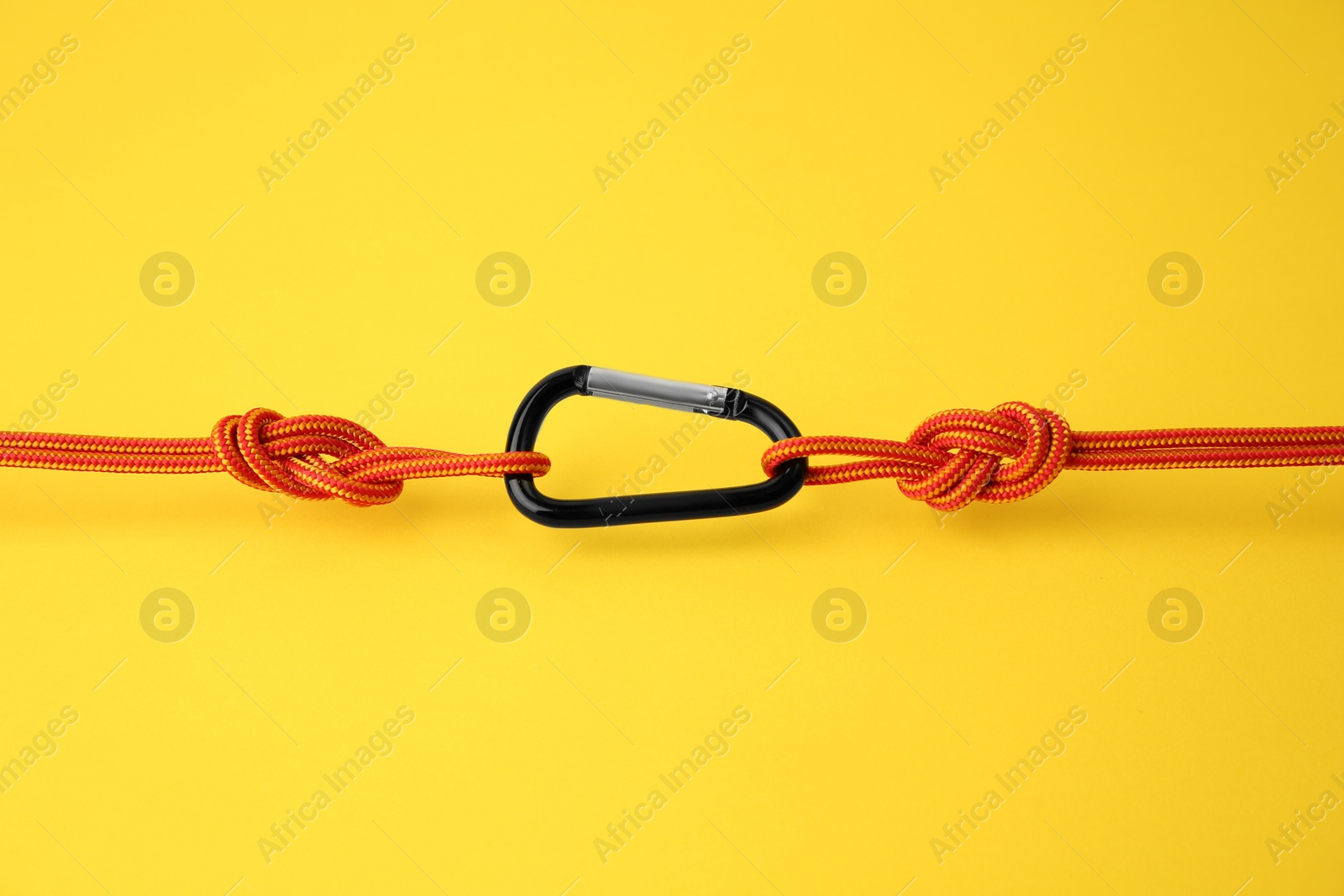 Photo of One metal carabiner with ropes on yellow background