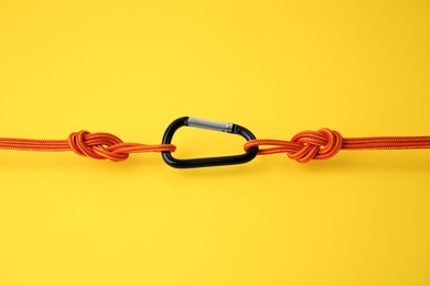 Photo of One metal carabiner with ropes on yellow background