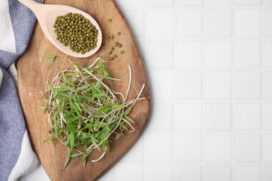 Photo of Wooden board with mung beans and sprouts on white tiled table, top view. Space for text