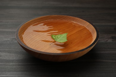 Photo of Bowl with water and green leaf on dark wooden table, closeup