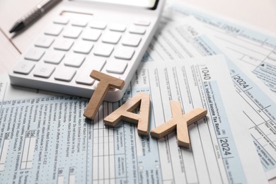 Word Tax made with wooden letters, calculator and documents on table, closeup