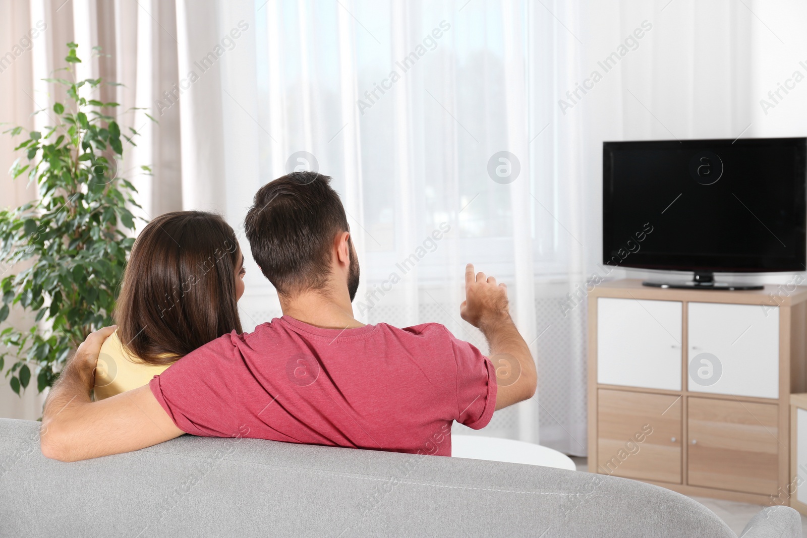 Photo of Young couple watching TV on sofa at home