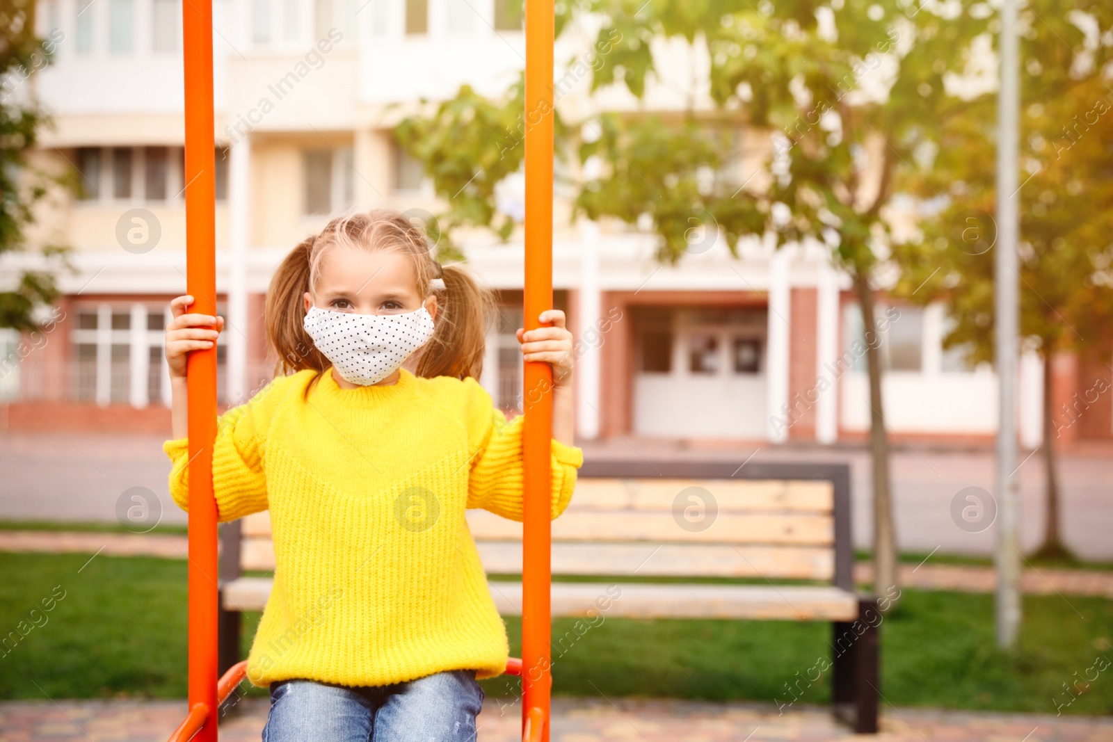 Photo of Little girl with medical face mask on playground during covid-19 quarantine