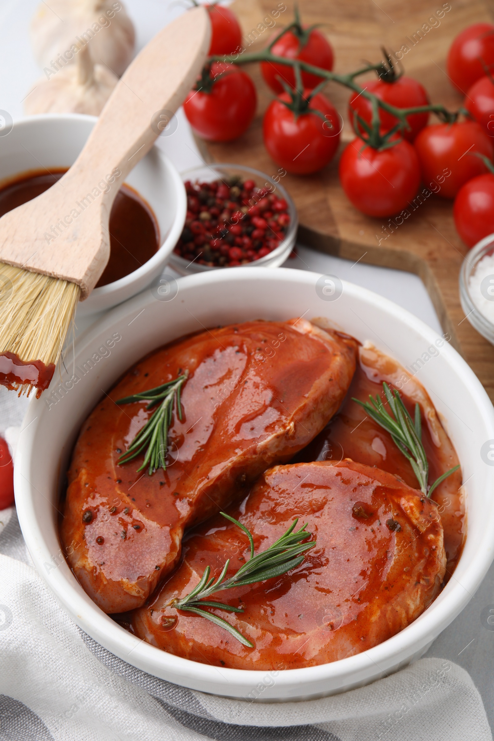 Photo of Raw marinated meat, rosemary and basting brush on table, closeup