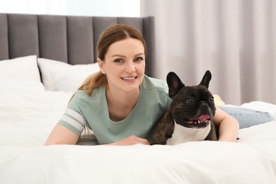 Happy woman hugging with cute French Bulldog on bed in room