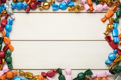 Frame of candies in colorful wrappers on beige wooden table, flat lay. Space for text