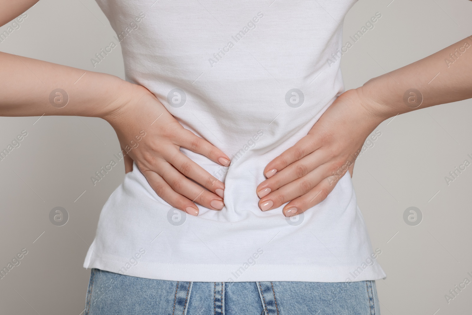 Photo of Woman suffering from back pain on light grey background, closeup. Arthritis symptoms