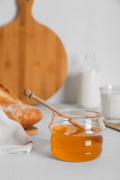 Jar with honey and bread on white table