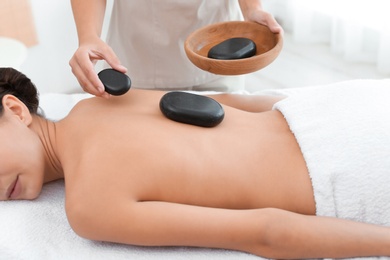 Photo of Beautiful young woman getting hot stone massage in spa salon