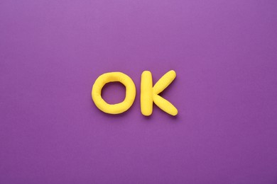 Photo of Word Ok made of yellow plasticine on purple background, top view