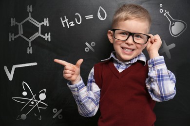Cute little child wearing glasses near chalkboard with chemical formulas
