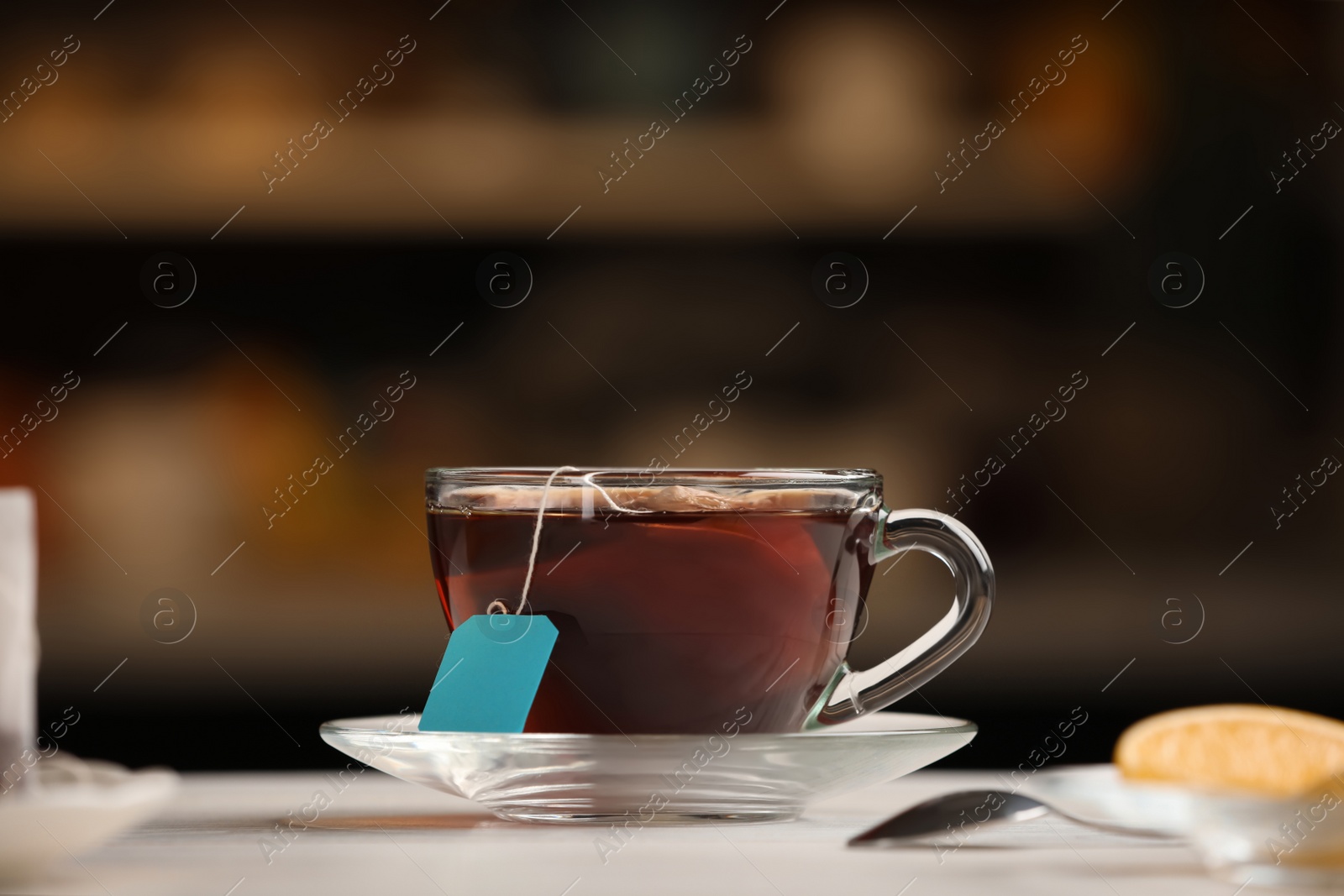 Photo of Tea bag in glass cup of hot water on white table against blurred background