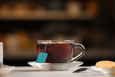 Photo of Tea bag in glass cup of hot water on white table against blurred background