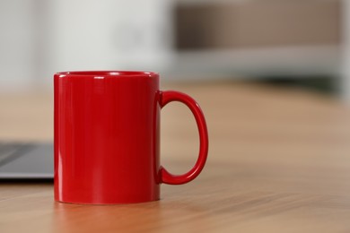 Photo of Red ceramic mug on wooden table at workplace. Space for text