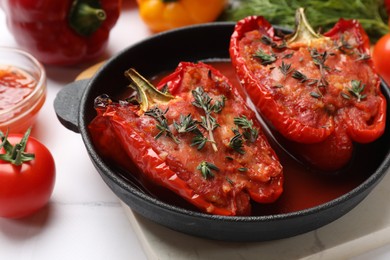 Photo of Tasty stuffed peppers in dish and ingredients on white tiled table, closeup