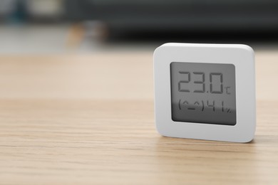 Photo of Digital hygrometer with thermometer on wooden table indoors. Space for text