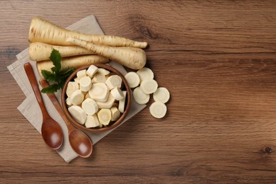 Photo of Flat lay composition with whole and cut fresh ripe parsnips on wooden table. Space for text