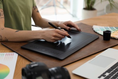 Professional designer with graphic tablet at wooden table, closeup