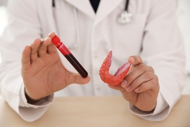 Photo of Doctor holding plastic model of thyroid and test tube with blood sample at wooden table, closeup