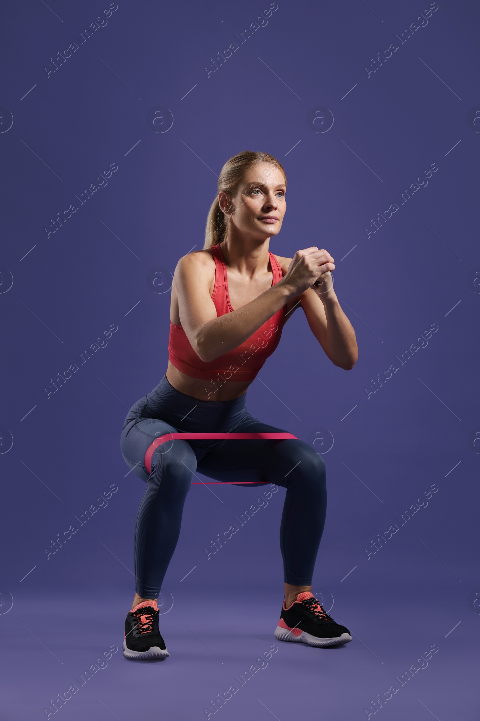 Photo of Athletic woman exercising with elastic resistance band on purple background