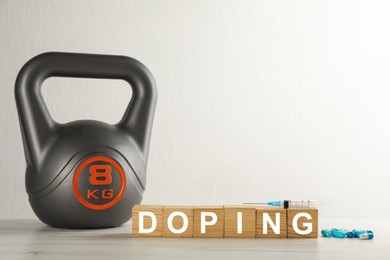 Photo of Wooden cubes with word Doping, drugs and kettlebell on table. Space for text
