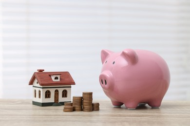 Photo of House model, piggy bank and stacked coins on wooden table