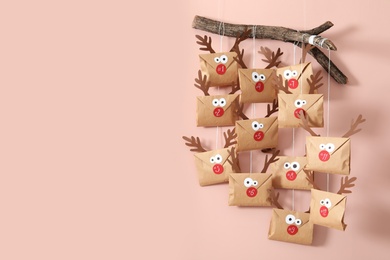 Photo of Gifts in envelopes with deer faces hanging on pink wall, space for text. Christmas advent calendar