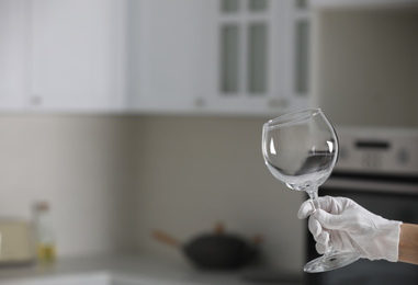 Person in white glove checking cleanliness of glass indoors, closeup. Space for text